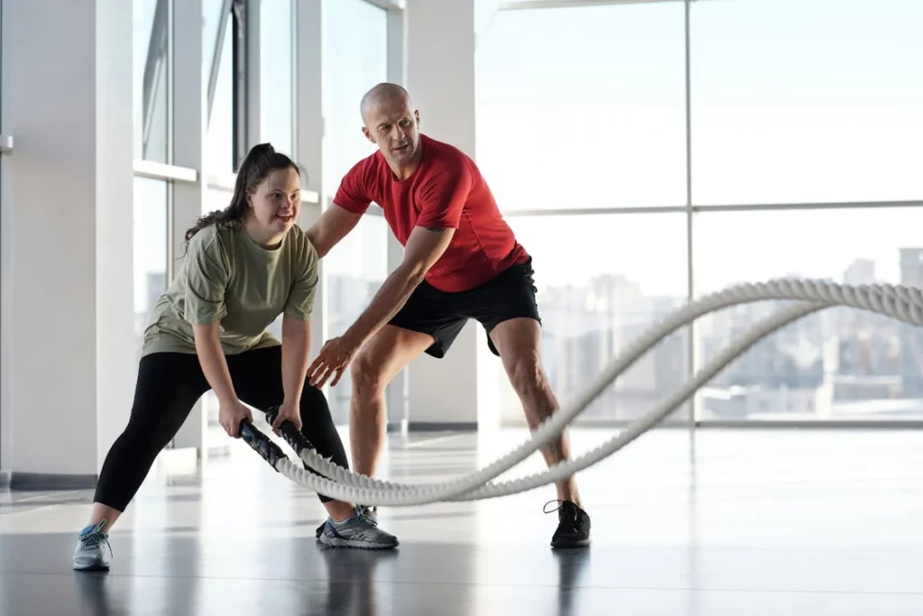 A Woman holding ropes and trainer guiding her in the gym