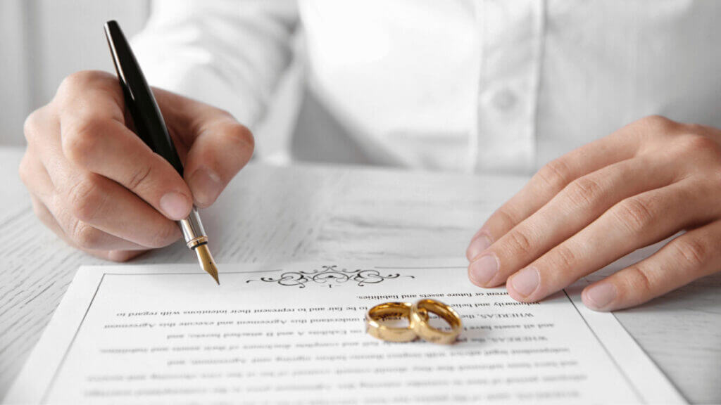 A person with a pen signing on a marriage certificate 