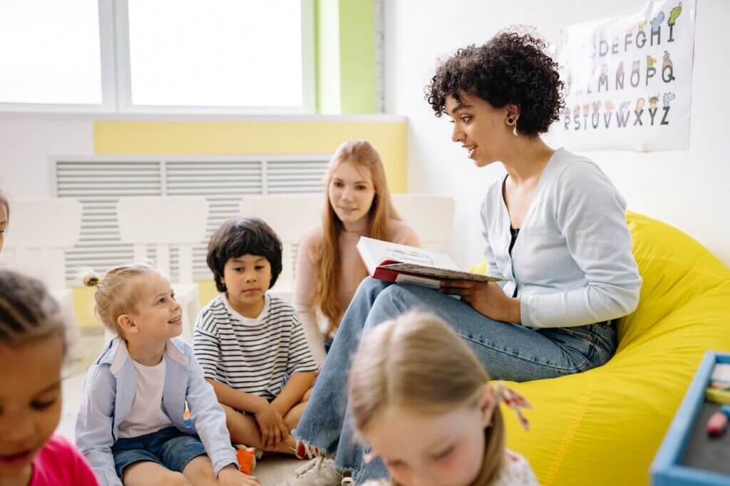 a teacher sitting on the sofa talking with her students in a class room.