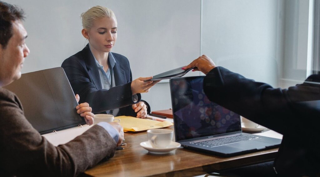 A businesswomen handing over file to his colleague while sitting in a business meeting