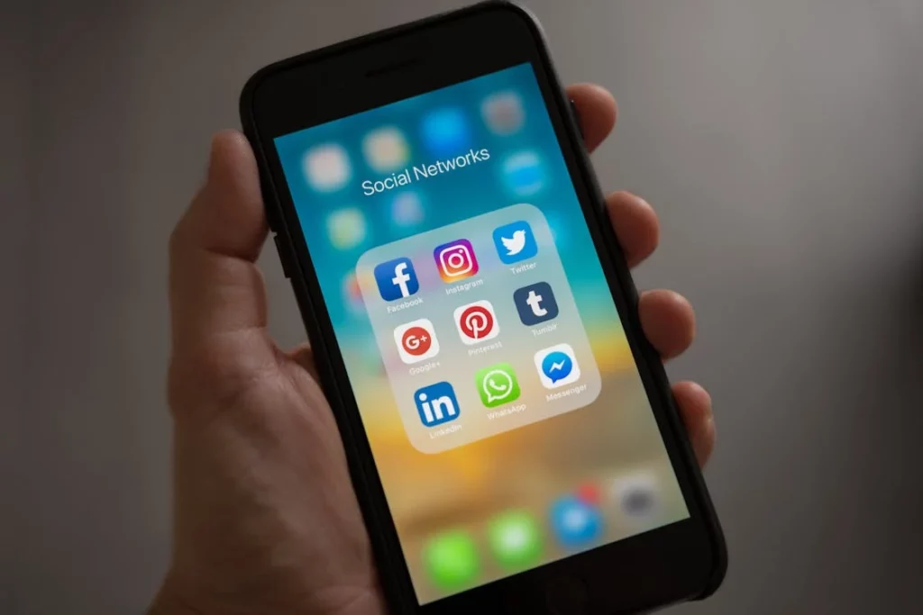 Person holding a phone and scree showing social networks including LinkedIn, Pinterest, WhatsApp, Messenger, Tumblr, Twitter, Instagram, and Facebook.